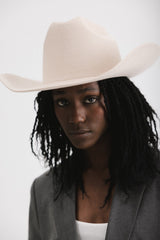 Person wearing a beige cowboy hat and gray blazer against a white background