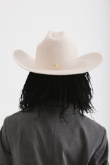 Person wearing a beige cowboy hat and dark coat on a white background