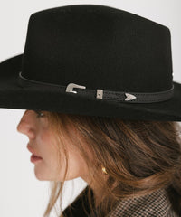 Black hat with a decorative band worn by a person on a white background