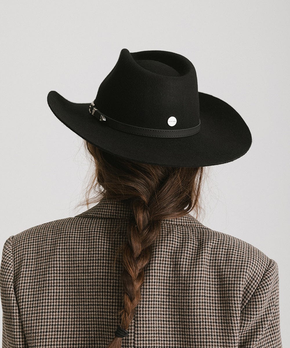 Person wearing a black cowboy hat with a white button on a plain background