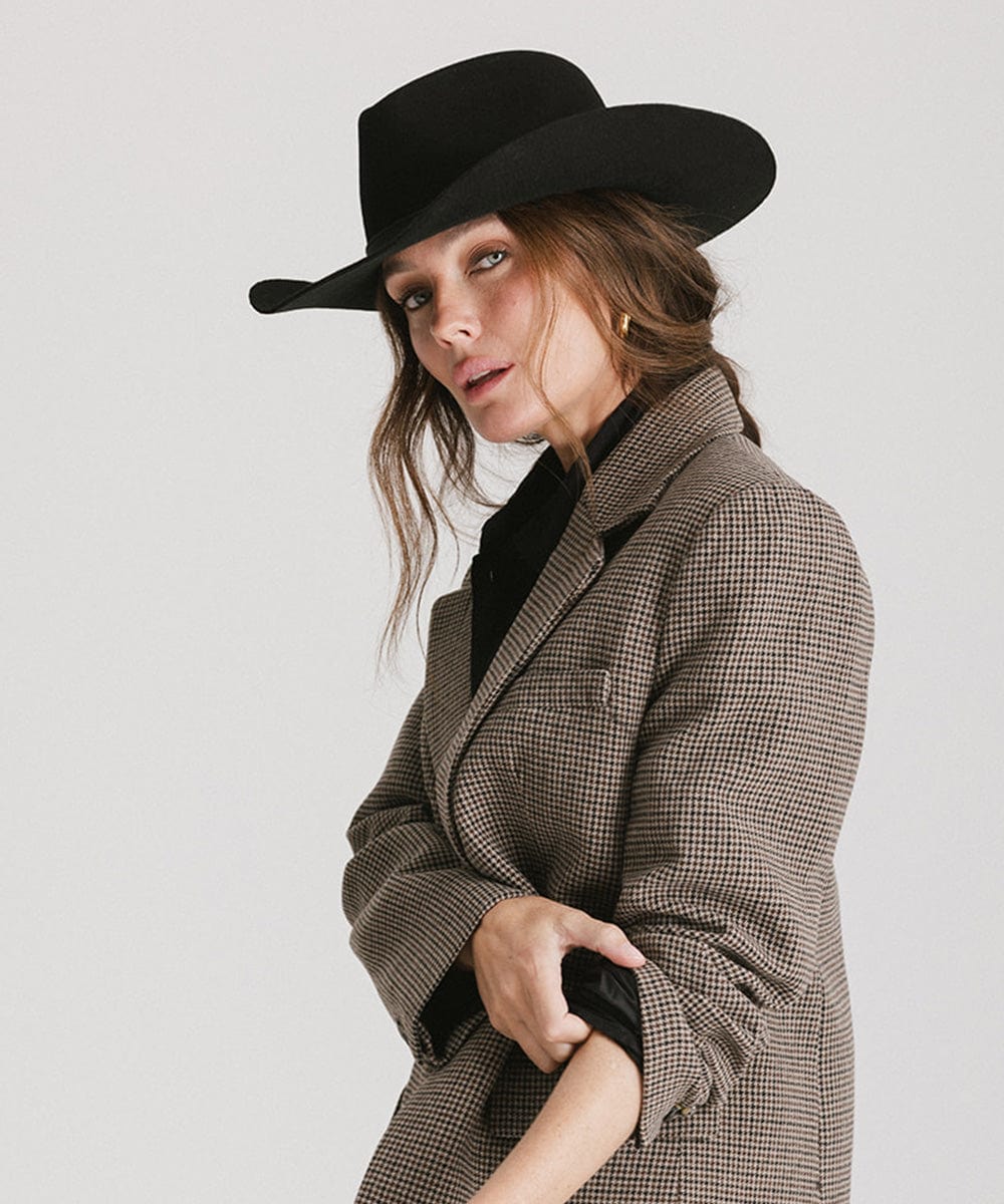 Woman wearing a black hat and brown checkered coat on a plain background