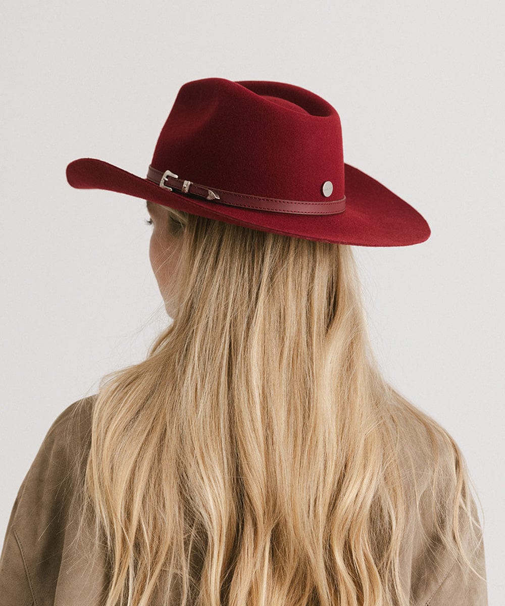 Red cowboy hat worn by a person with blonde hair on a plain background