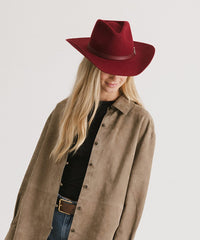 Person wearing a red fedora hat and brown coat on a plain background