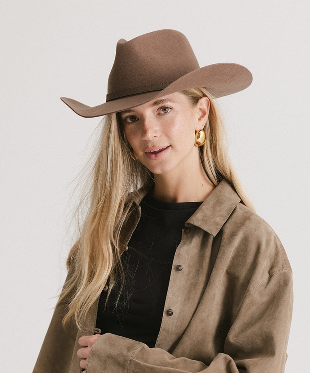 Woman wearing a brown cowboy hat and coat on a plain background