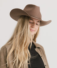 Woman wearing a brown cowboy hat and beige coat on a plain background