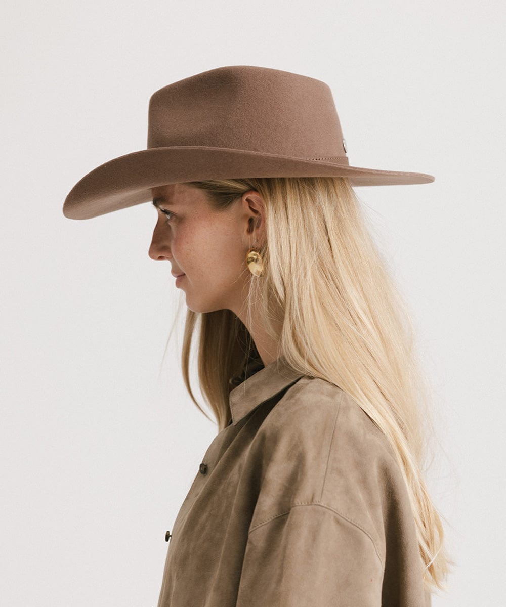 Person wearing a brown wide-brimmed hat and beige jacket on a white background