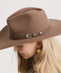 Brown cowboy hat with decorative band worn by a person on a white background