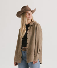 Woman wearing a brown cowboy hat and jacket on a plain background