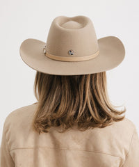 Person wearing a beige cowboy hat and jacket on a white background