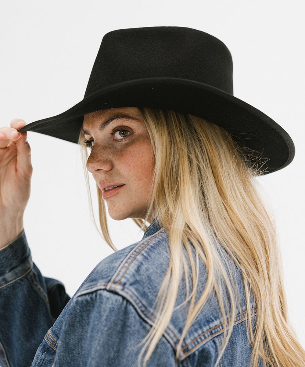 Woman wearing a black hat and denim jacket on a plain background