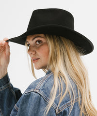 Woman wearing a black hat and denim jacket on a plain background