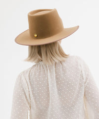 Person wearing a brown hat and white polka dot shirt on a light gray background