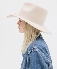 Person wearing a beige wide-brimmed hat and denim jacket on a white background