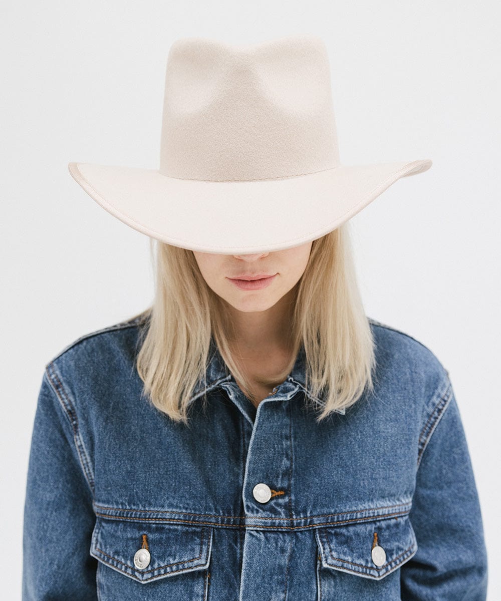 Person wearing a beige hat and denim jacket on a white background