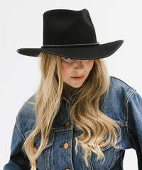 Person wearing a black hat and denim jacket on a white background
