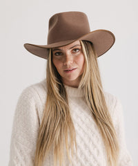 Woman wearing a brown hat and white sweater against a plain background