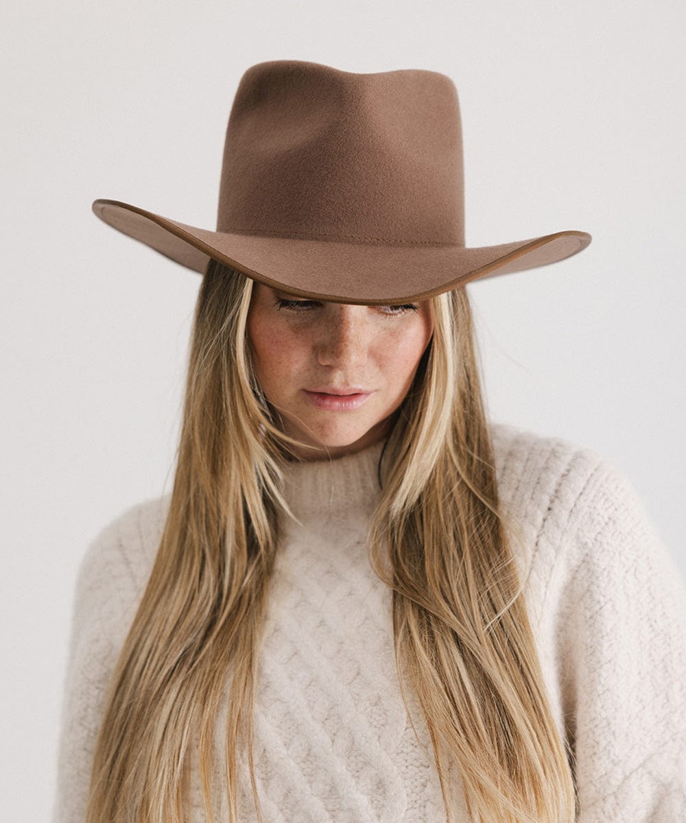 Person wearing a brown wide-brimmed hat and beige sweater against a white background