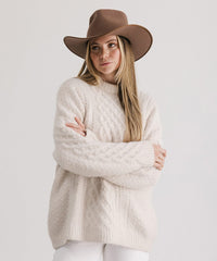 Woman wearing a beige sweater and brown hat against a white background