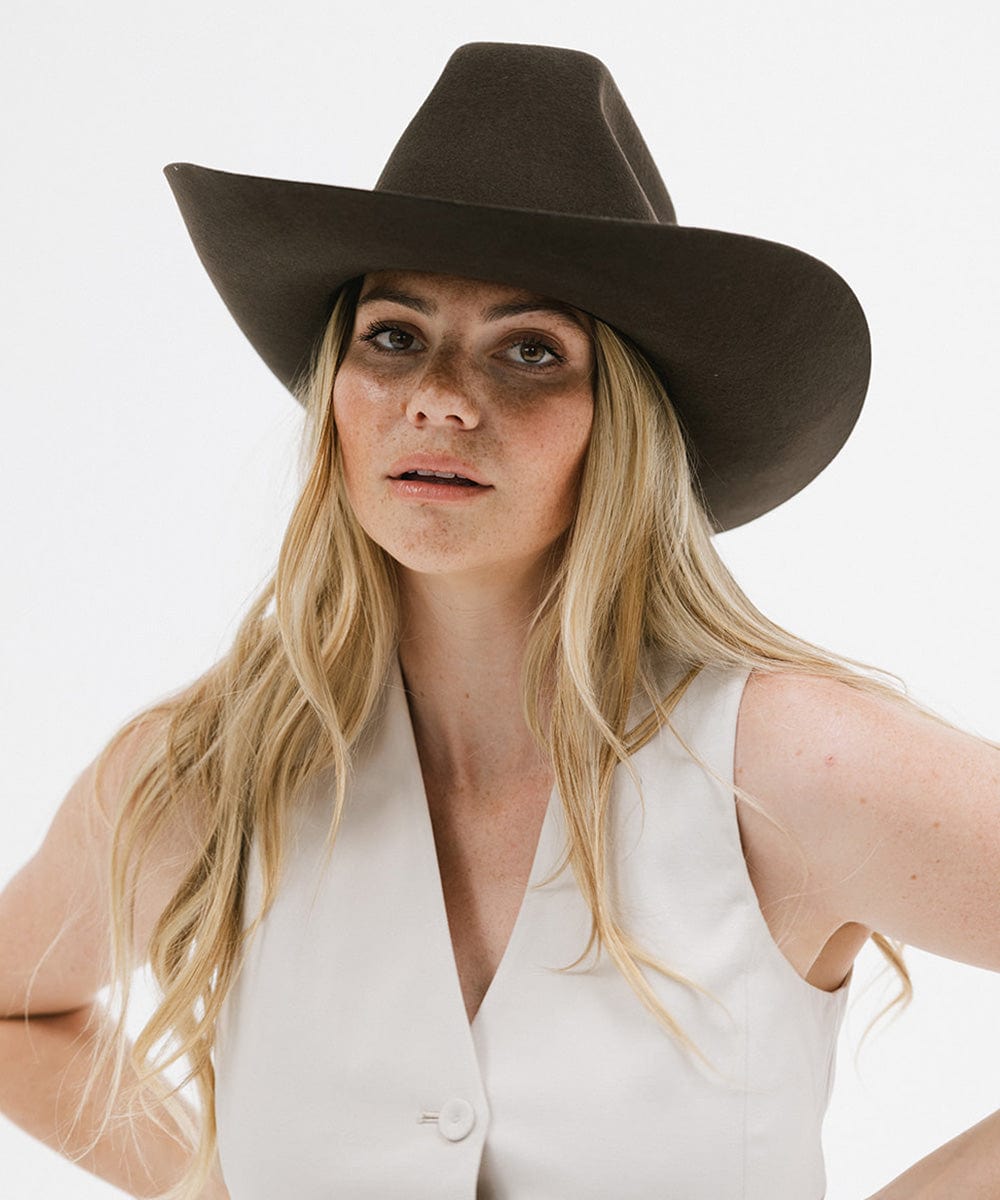 Woman wearing a brown cowboy hat and white sleeveless top on a light background