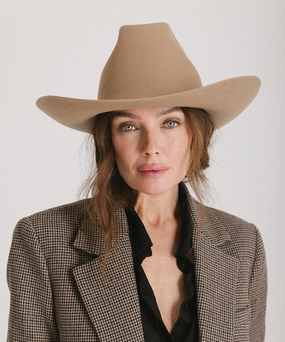 Woman wearing a beige cowboy hat and checkered blazer on a white background