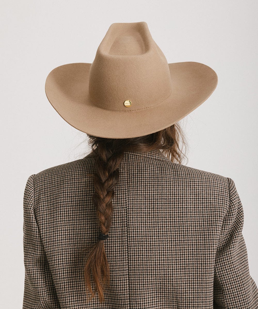 Person wearing a brown cowboy hat and checkered blazer with braided hair on a white background