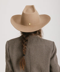 Person wearing a brown cowboy hat and checkered blazer with braided hair on a white background
