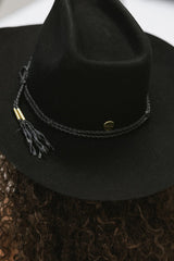Black cowboy hat with a braided band and tassel on a textured surface
