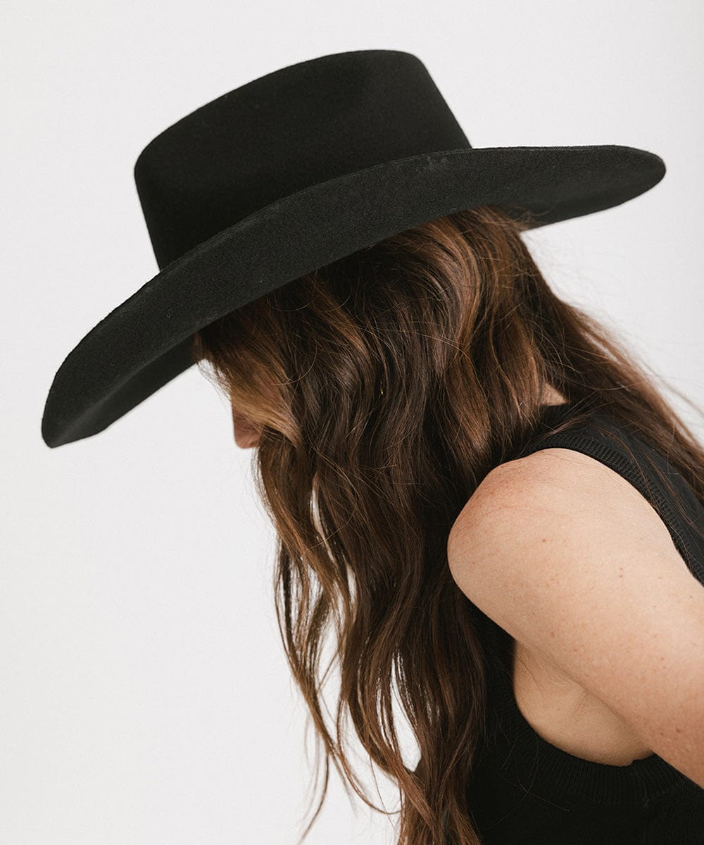 Person wearing a black wide-brimmed hat with long hair on a white background