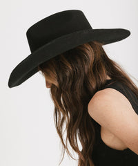 Person wearing a black wide-brimmed hat with long hair on a white background