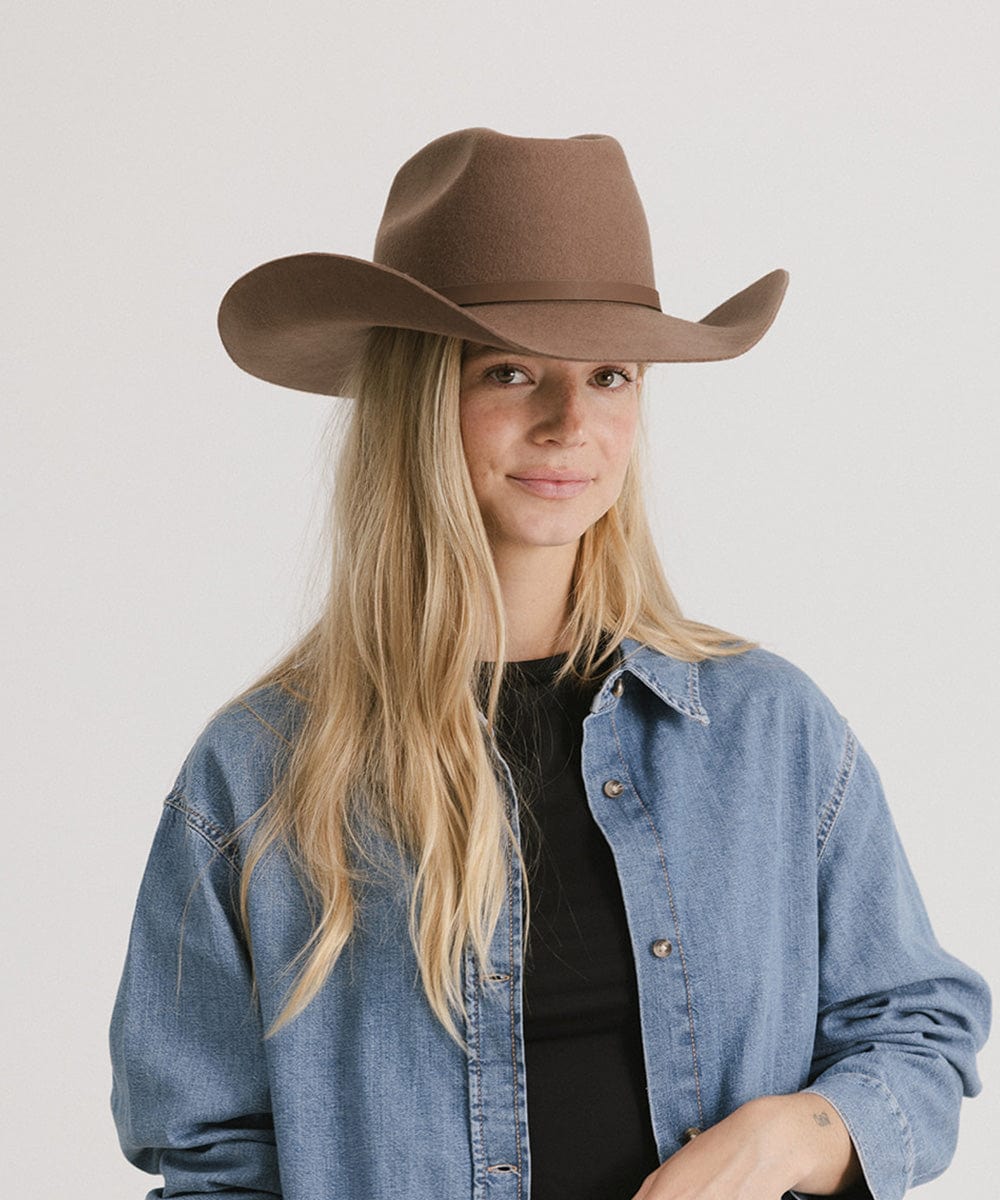 Woman wearing a brown cowboy hat and denim jacket on a plain background