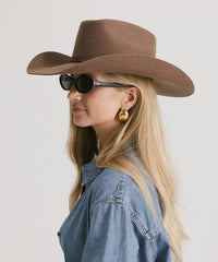 Woman wearing a brown cowboy hat and denim jacket on a plain background