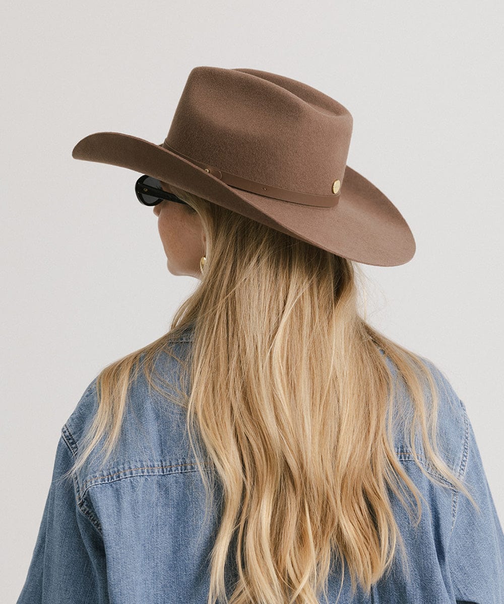 Person wearing a brown cowboy hat and denim jacket on a plain background
