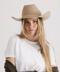 Woman wearing a beige cowboy hat and white t-shirt on a plain background