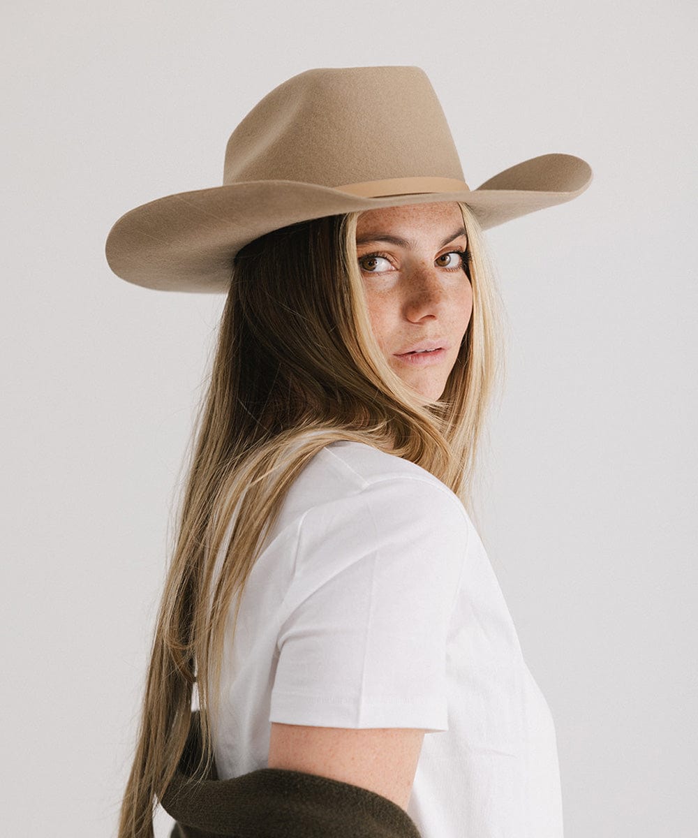 Woman wearing a beige cowboy hat against a plain background