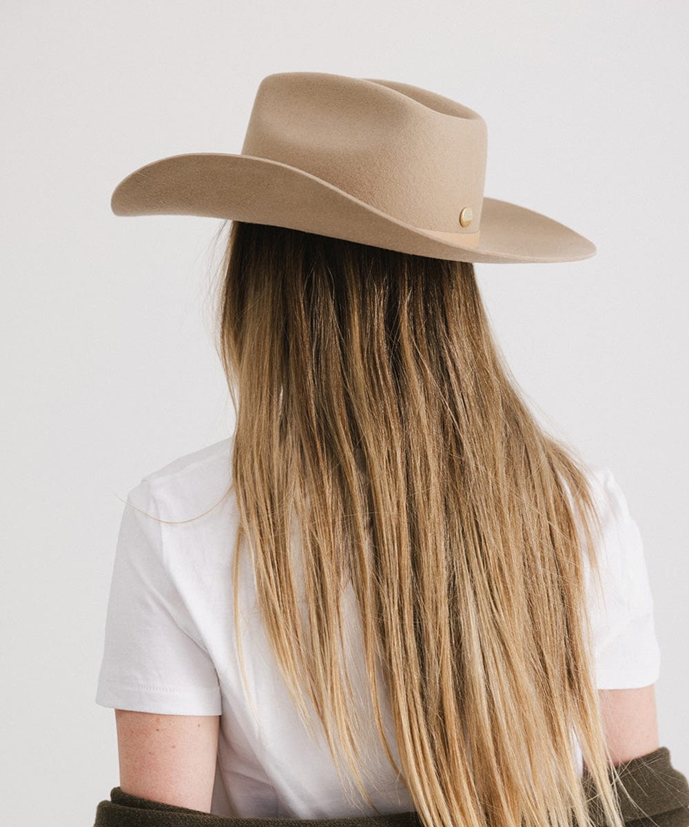 Person wearing a beige cowboy hat with long blonde hair on a white background