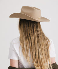 Person wearing a beige cowboy hat with long blonde hair on a white background