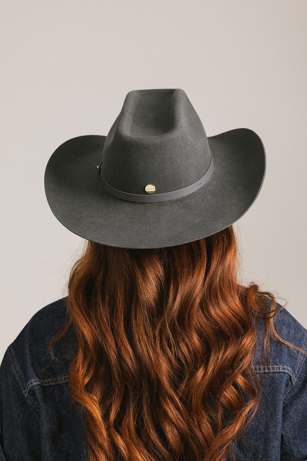 Person wearing a dark gray cowboy hat with a plain background