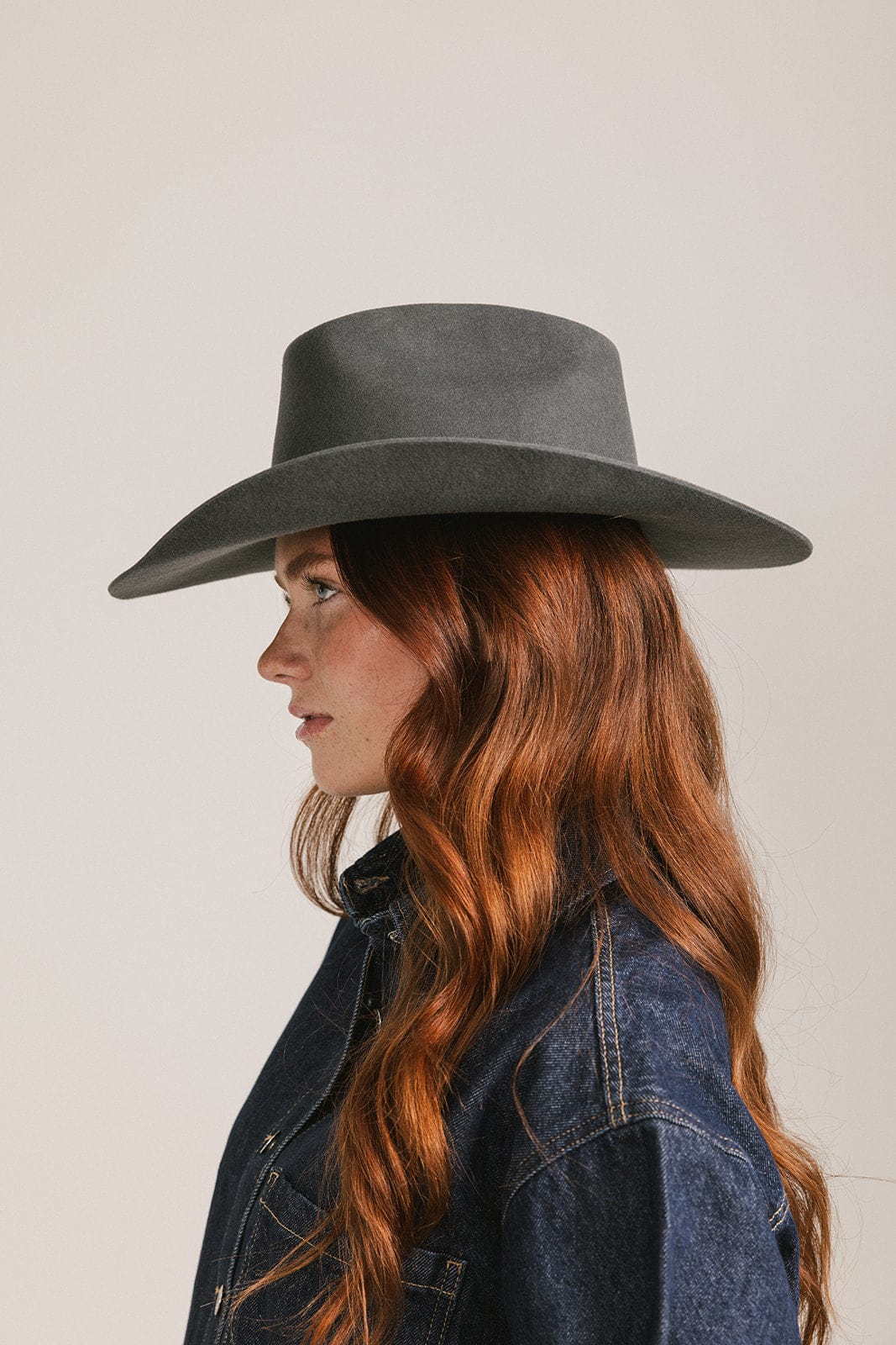 Woman wearing a gray wide-brimmed hat and denim jacket on a plain background