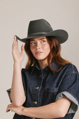 Woman wearing a dark gray wide-brimmed hat and denim shirt against a plain background