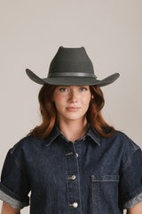 Woman wearing a dark gray fedora hat and denim shirt against a plain background