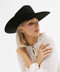 Woman wearing a black hat and white polka dot blouse against a white background