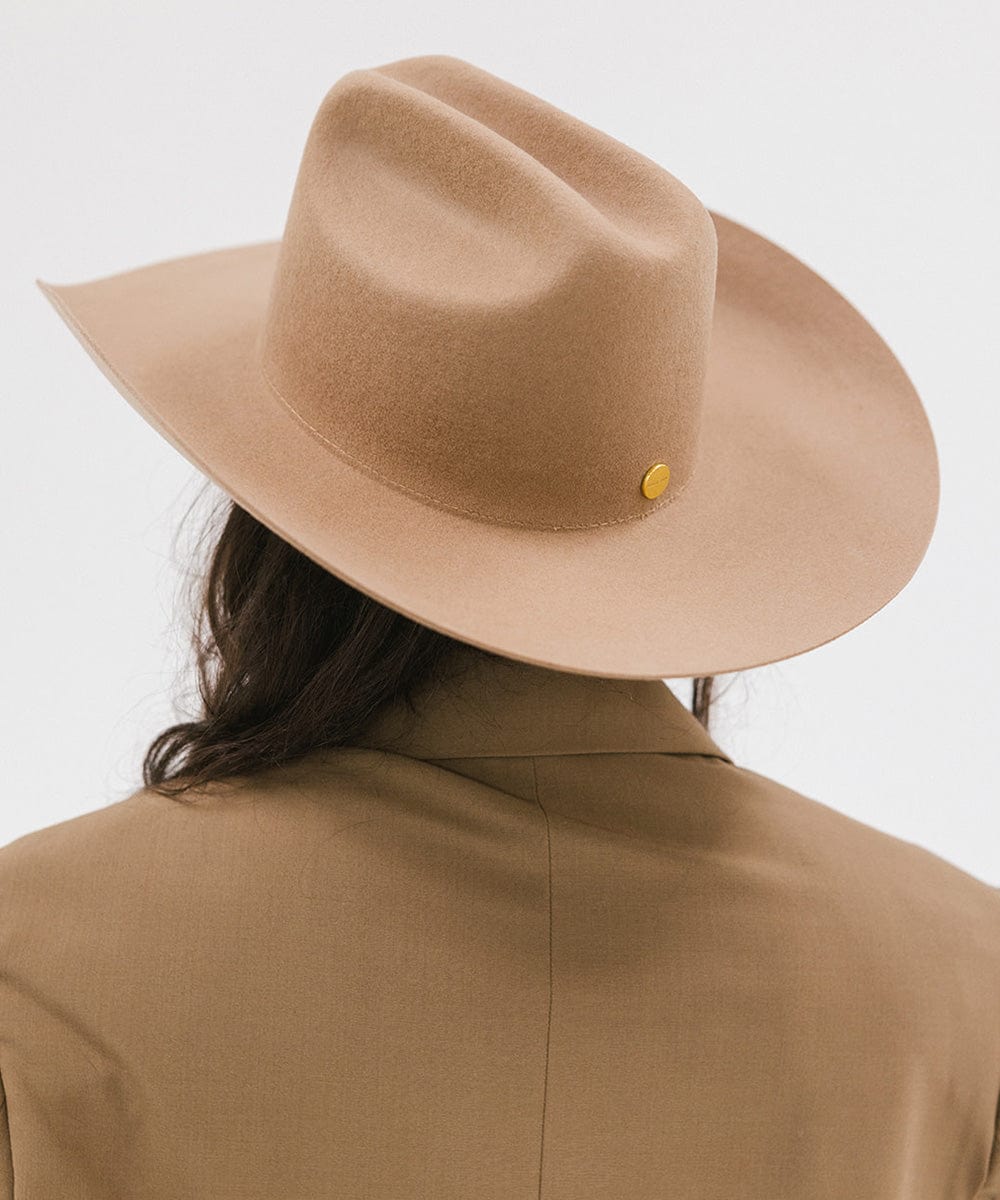 Person wearing a beige fedora hat with a yellow button on a white background