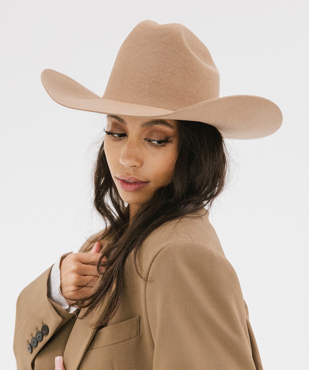 Woman wearing a beige cowboy hat and coat on a white background