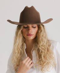 Woman wearing a brown cowboy hat against a plain background