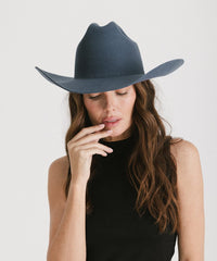 Woman wearing a wide-brimmed gray hat against a white background