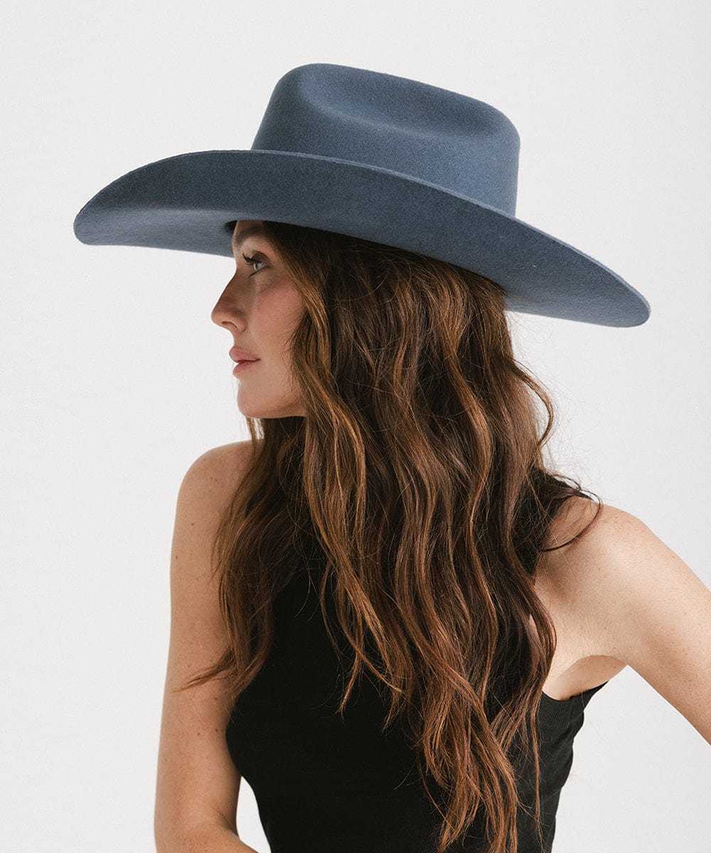 Woman wearing a wide-brimmed blue hat against a white background