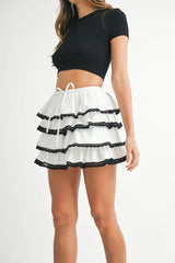 Woman wearing a black crop top and white skirt with black ruffles on a white background