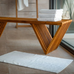 Stack of white towels on a wooden bench with a white bath mat in front