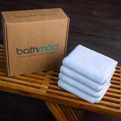 Stack of light blue towels next to a cardboard box with 'bathmod' branding on a wooden surface.