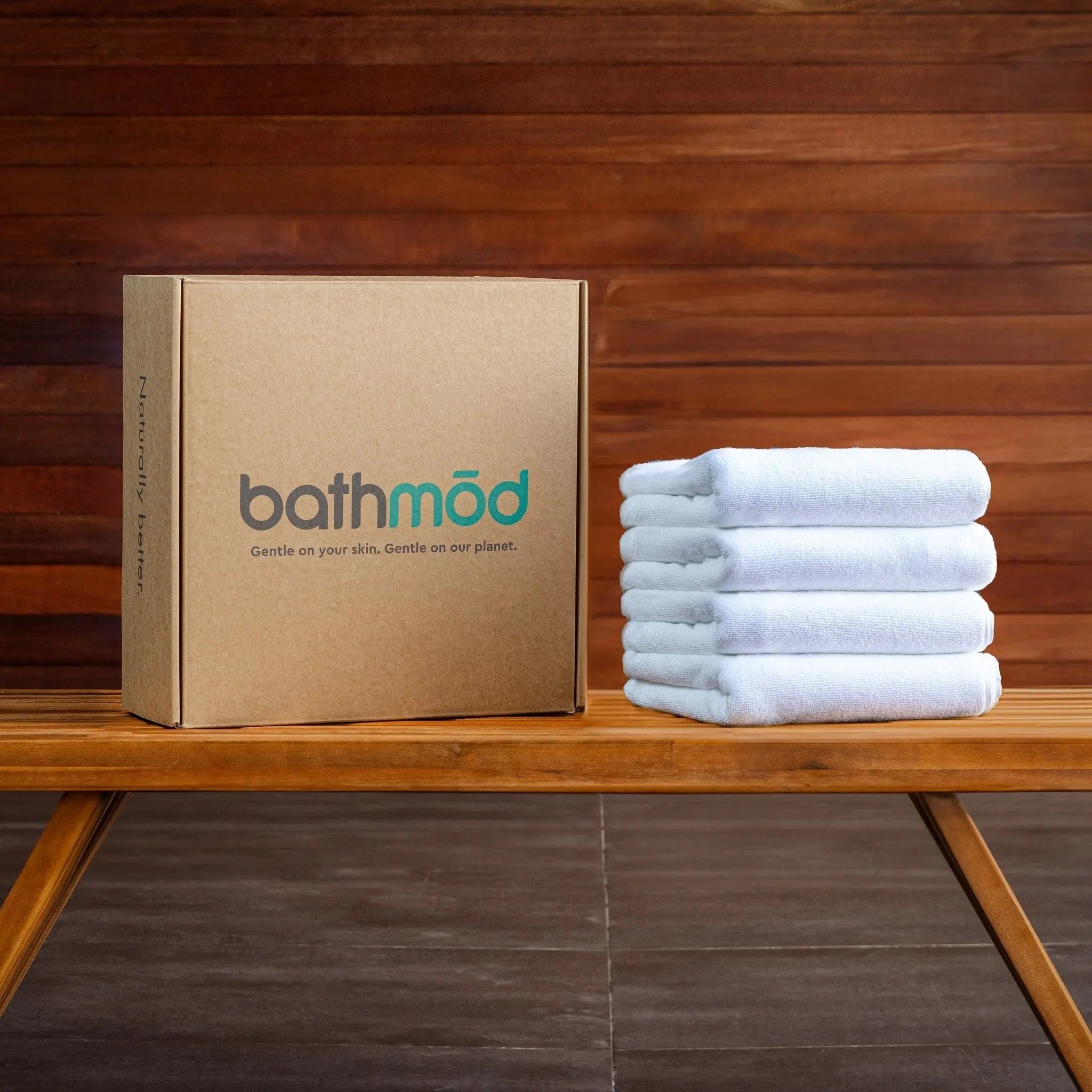 Stack of white towels next to a cardboard box with 'bathmöd' branding on a wooden surface.